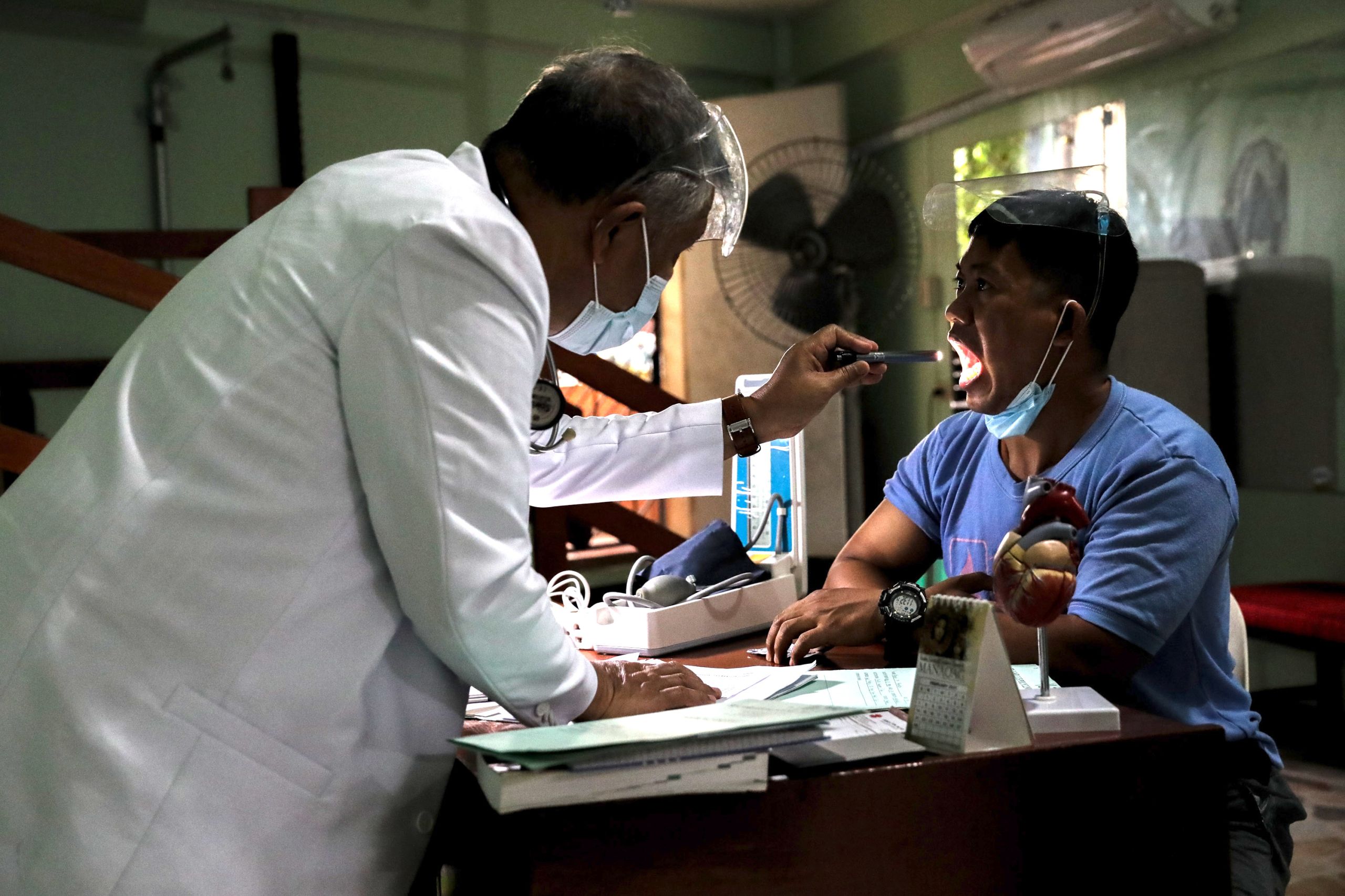 A doctor uses a flashlight to check on his patient inside a clinic.
