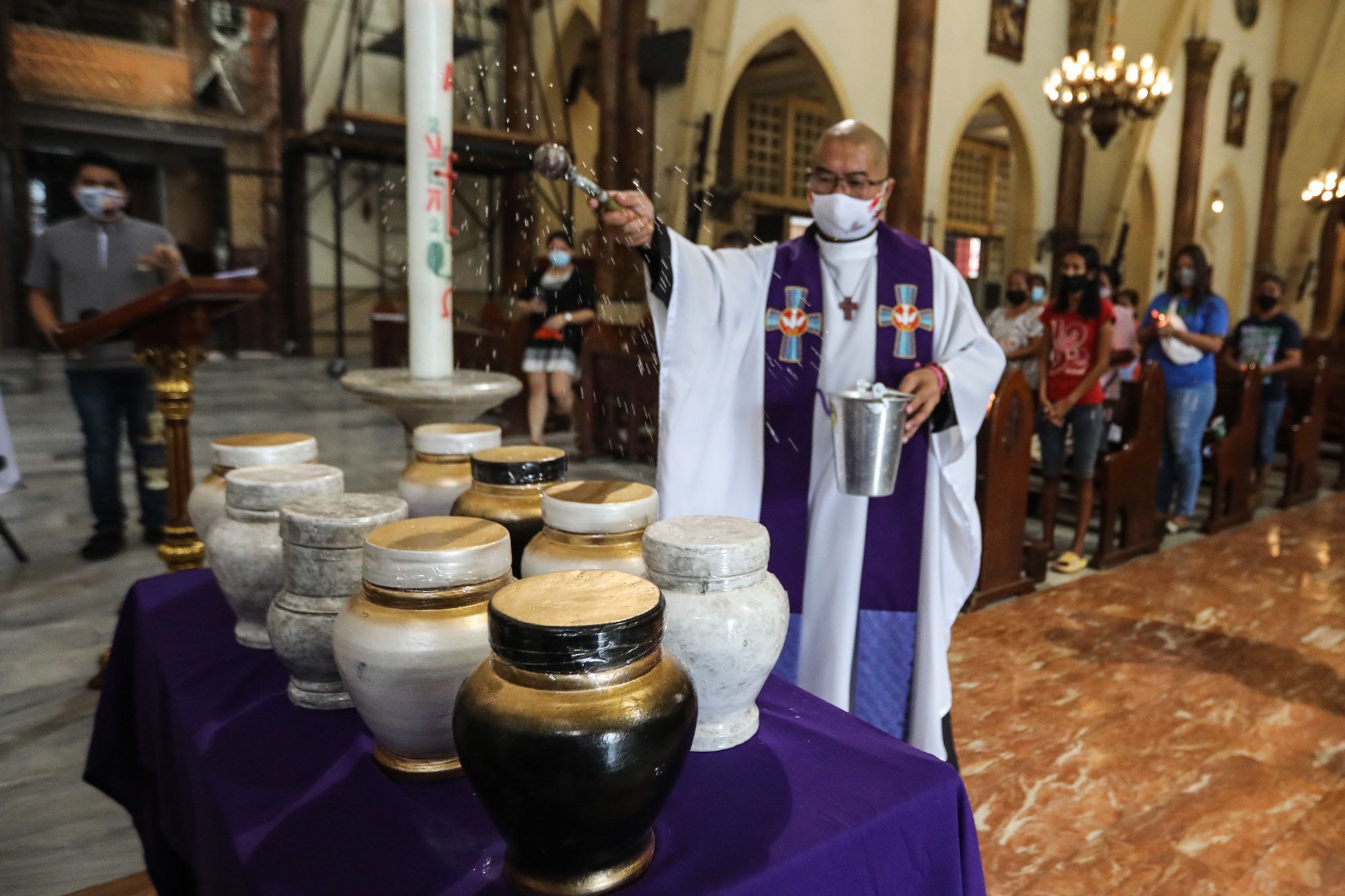A Catholic priest blessing a 9 urns containing ashes