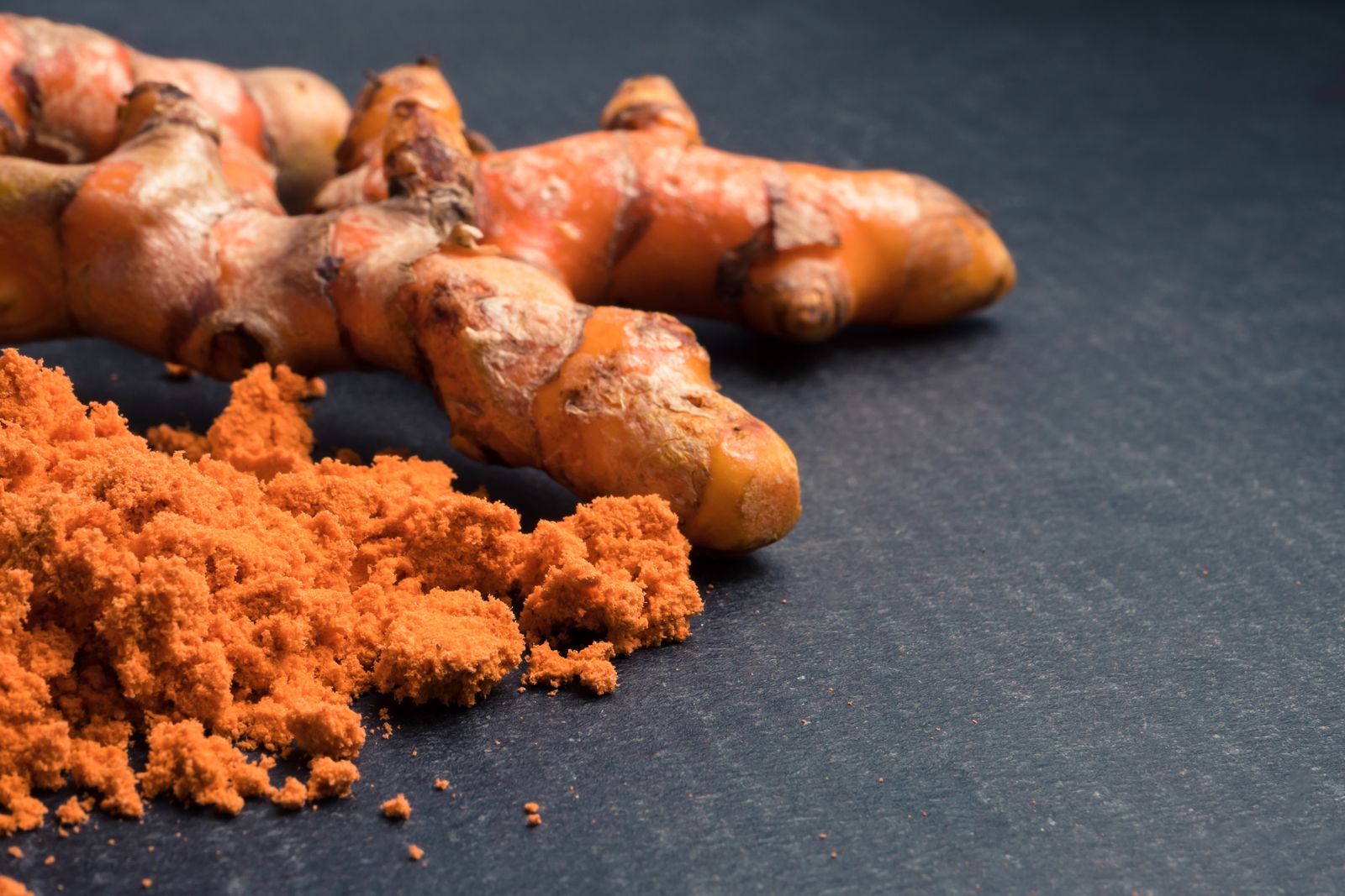 Turmeric roots with turmeric powder on black background