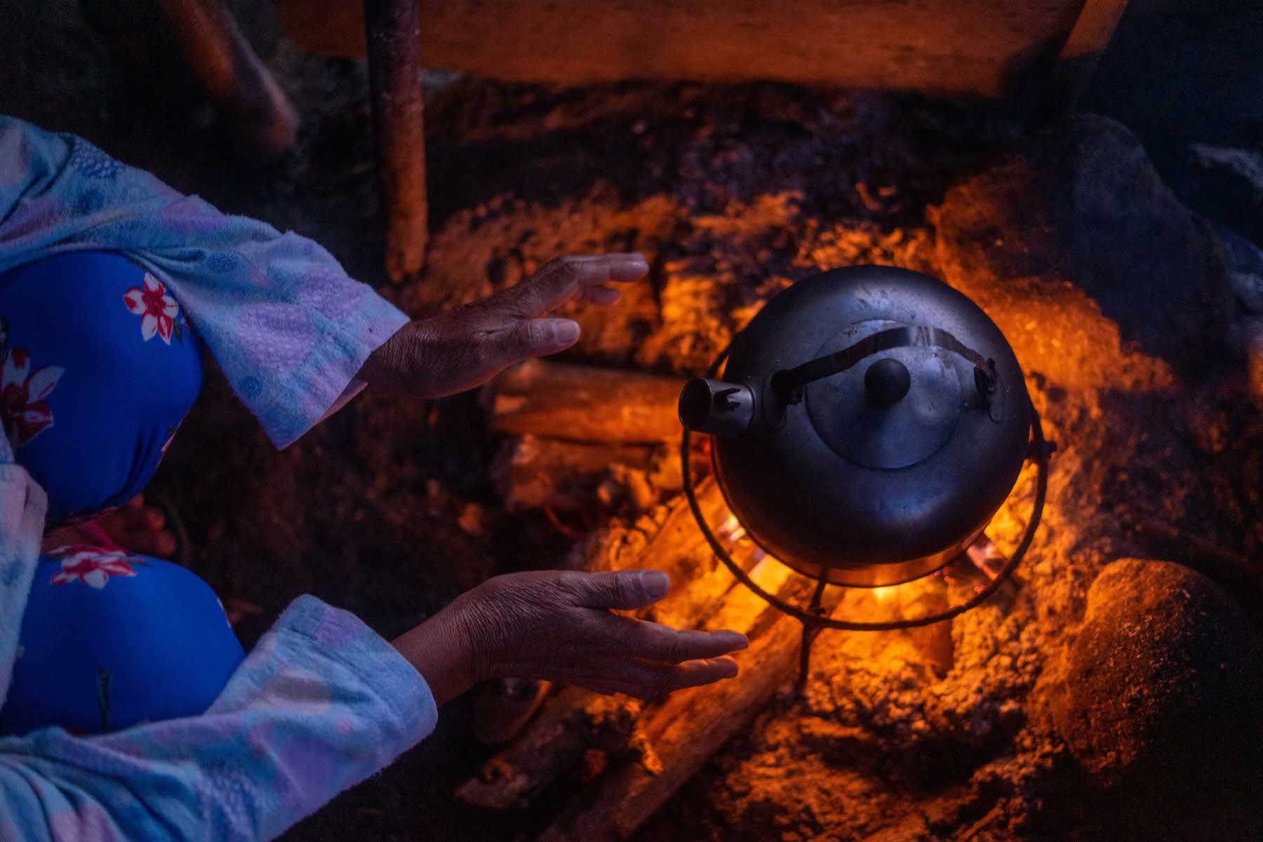 Woman's hand reaching for a pot over an open fire.