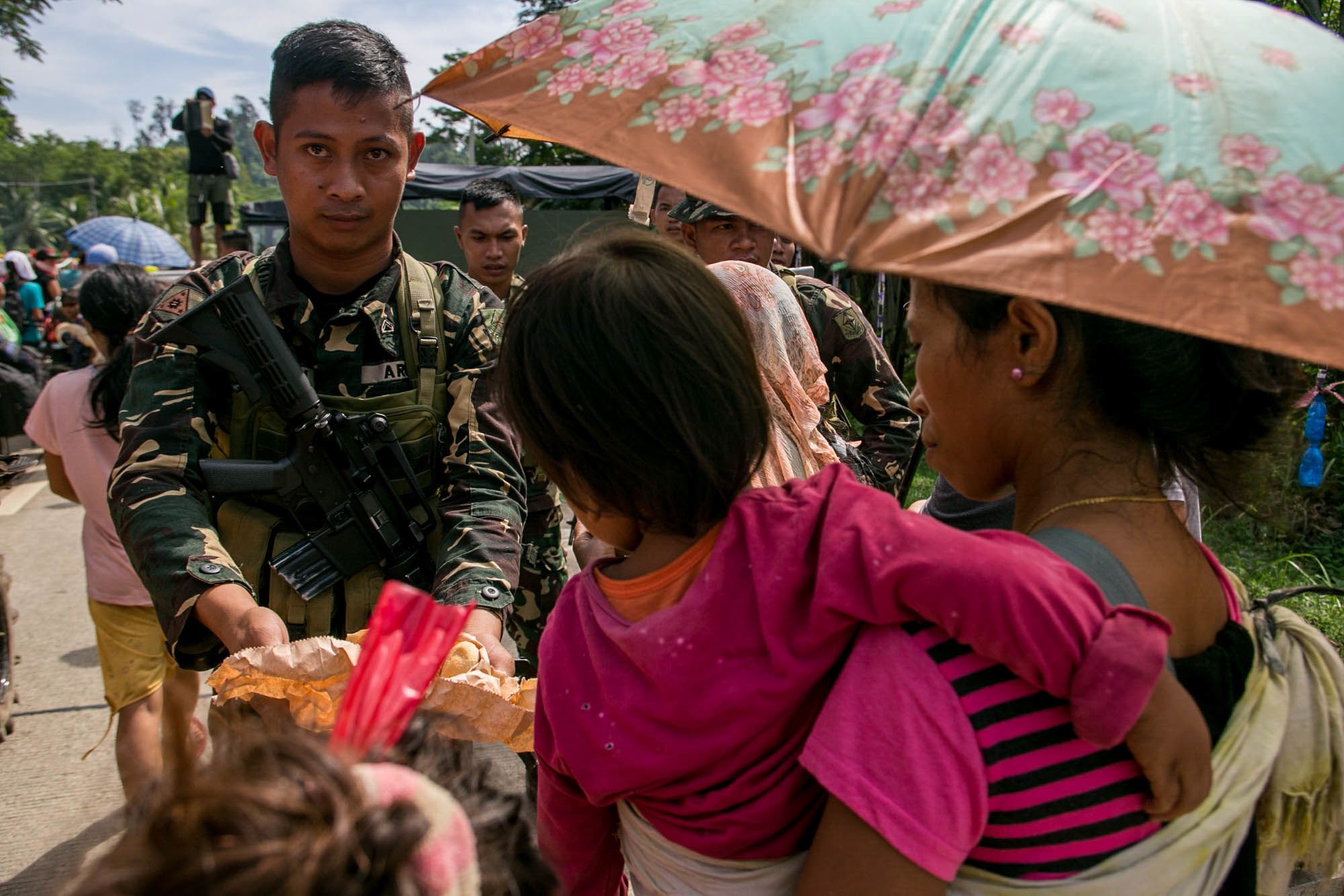An army trooper offers food to displaced indigenous people who started a journey to seek safer grounds in Surigao del Sur province in this photograph taken in 2018.