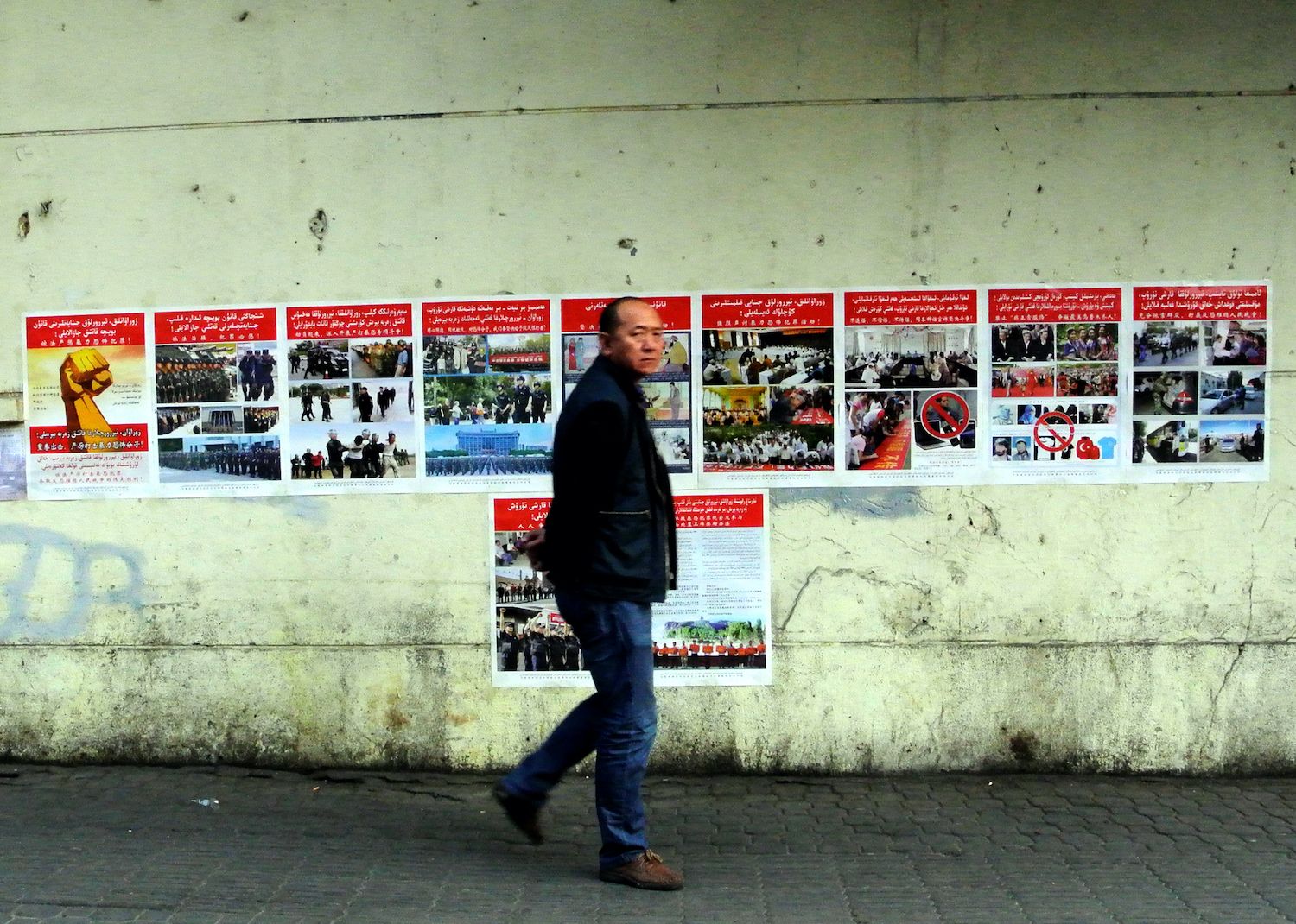 A pedestrian walks past anti-terror propaganda posters pasted along the streets of Urumqi,