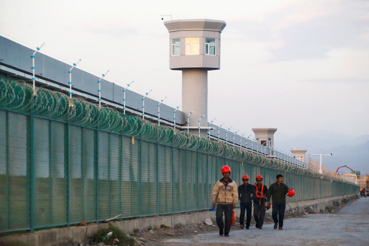 Workers walk by a perimeter fence in Xinjiang